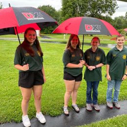 a group of young ham radio operators standing under umbrellas outside in the rain