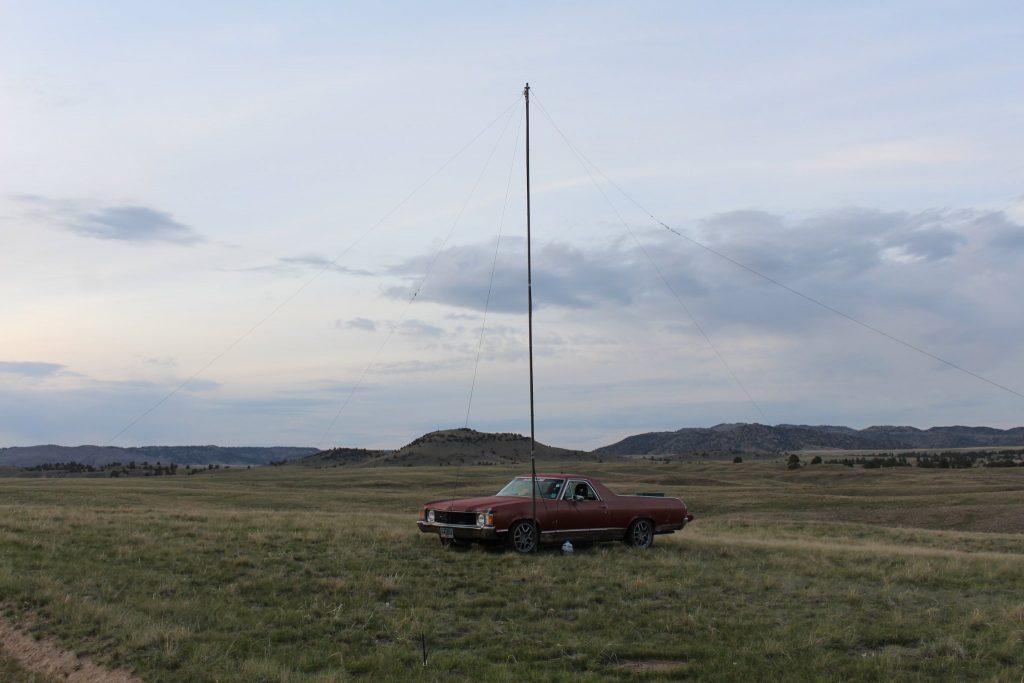 Chevy El Camino parked in desert plain next to radio antenna